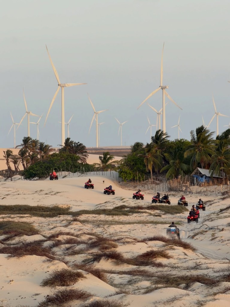 Comboio de quadriciclos na praia ampla com bangalôs de palha e dunas