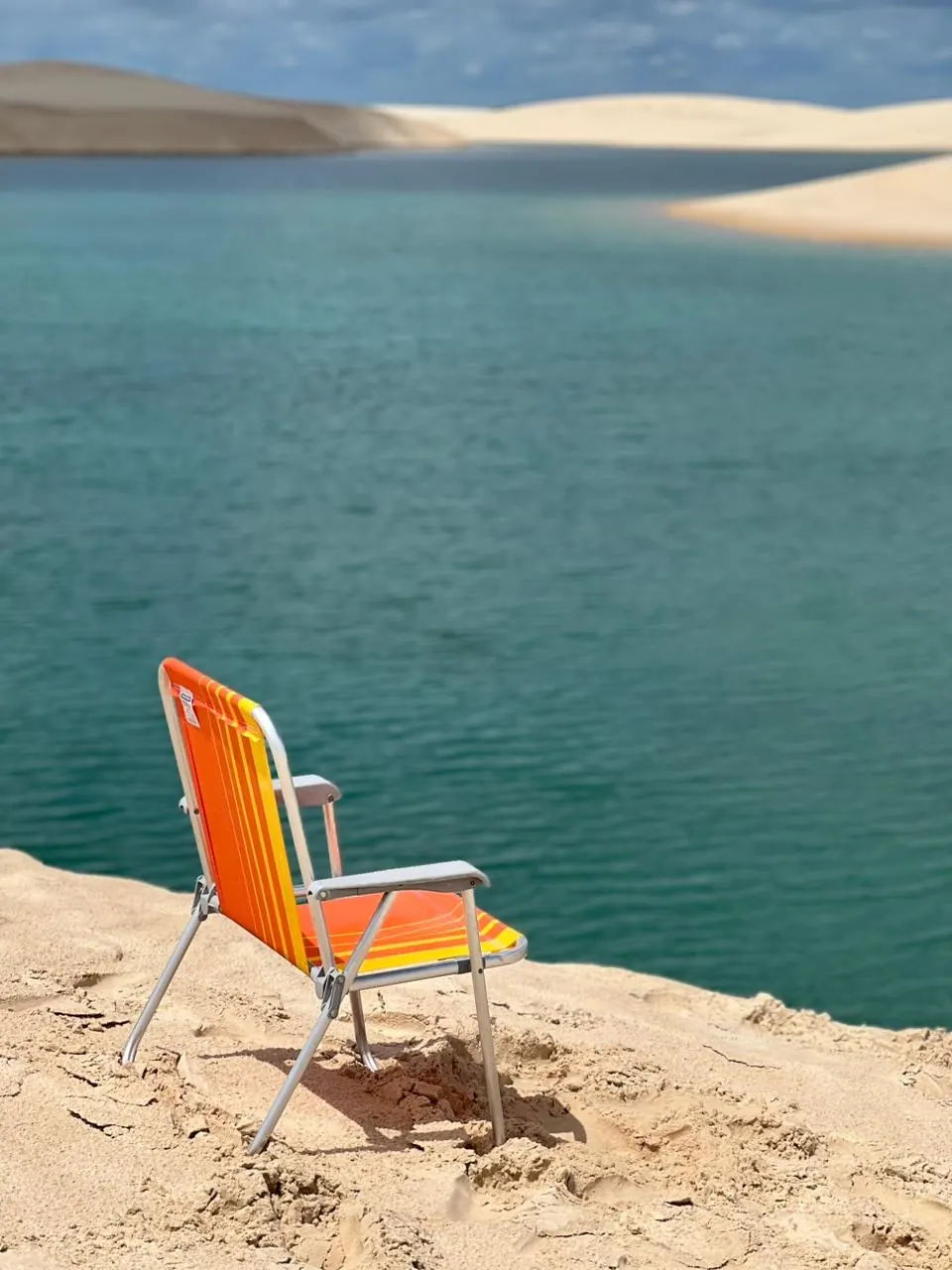 Cadeira de praia na beira de uma lagoa, com as dunas ao fundo