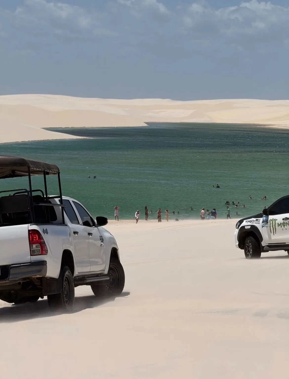 Caminhonetes 4x4 nas dunas brancas em frente a uma lagoa, com visitantes tomando banho