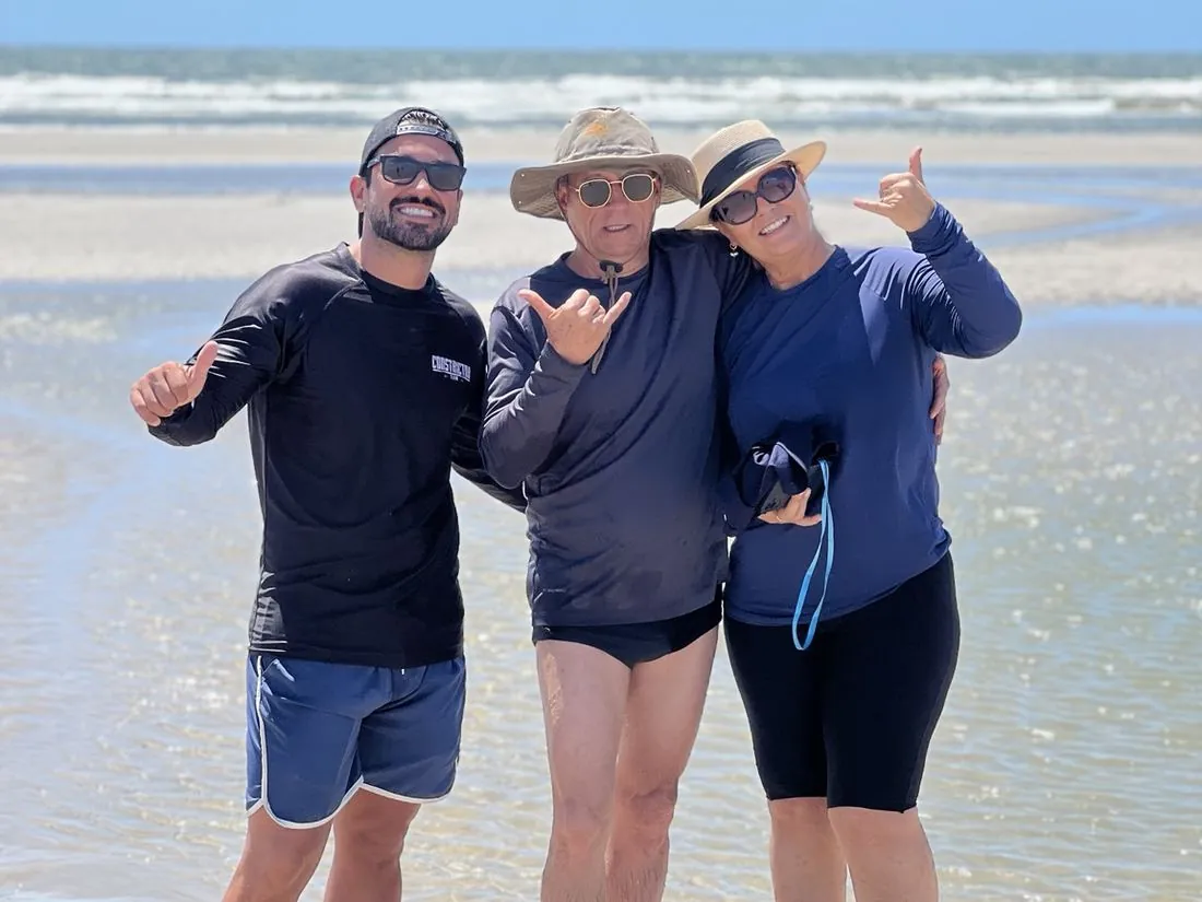 Três visitantes sorrindo na praia de Atins, com o mar ao fundo