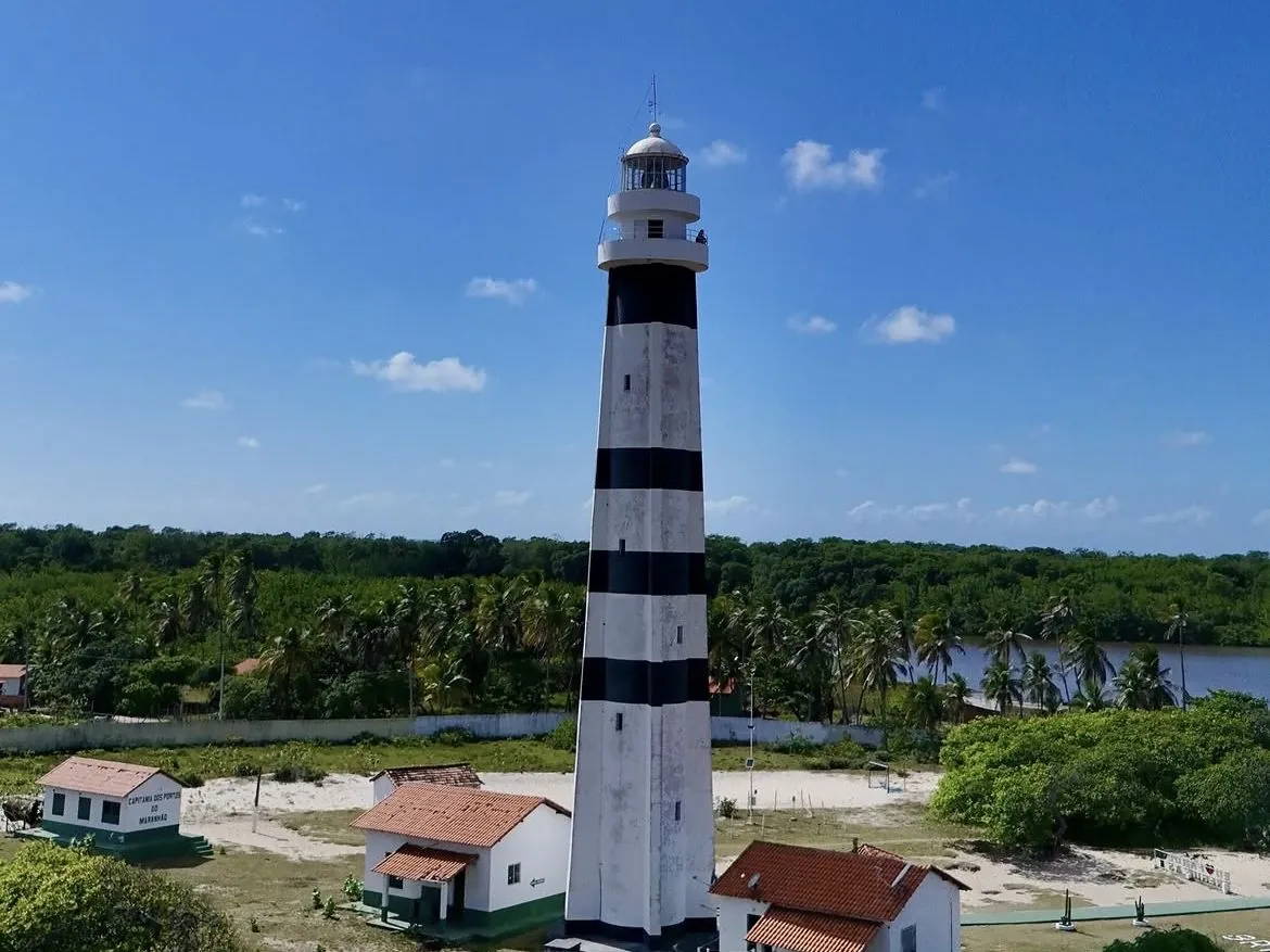 Mandacaru lighthouse seen from above, surrounded by coconut palms with the Preguiças River in the background