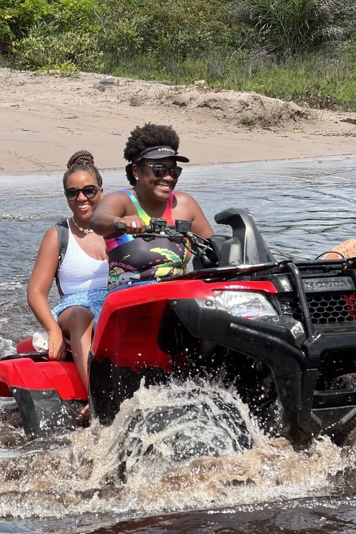 Two guests smiling on an ATV as they cross a stretch of water