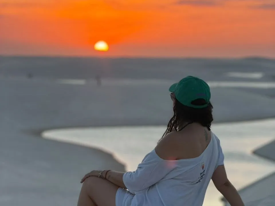 Pôr do sol na Lagoa Bonita, com visitante sentada no alto das dunas dos Lençóis Maranhenses