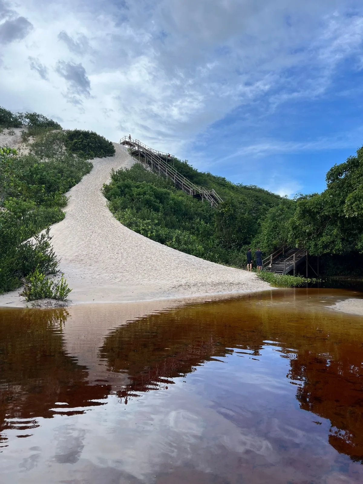 The climb up the Lagoa Bonita dune, with the wooden staircase and the dark-water lagoon reflecting the sky