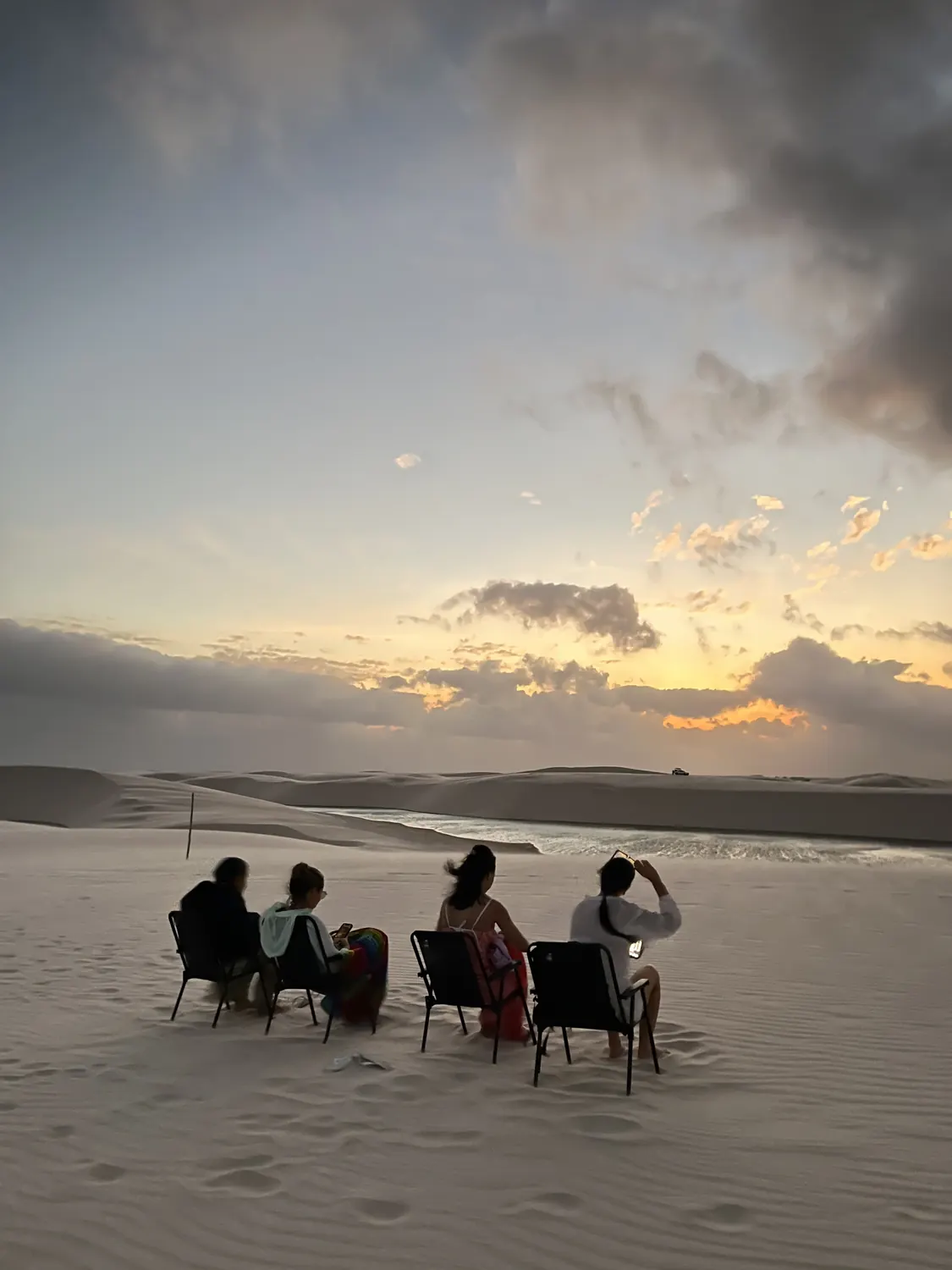 Cadeiras montadas na duna de frente para a lagoa, com o céu clareando no amanhecer