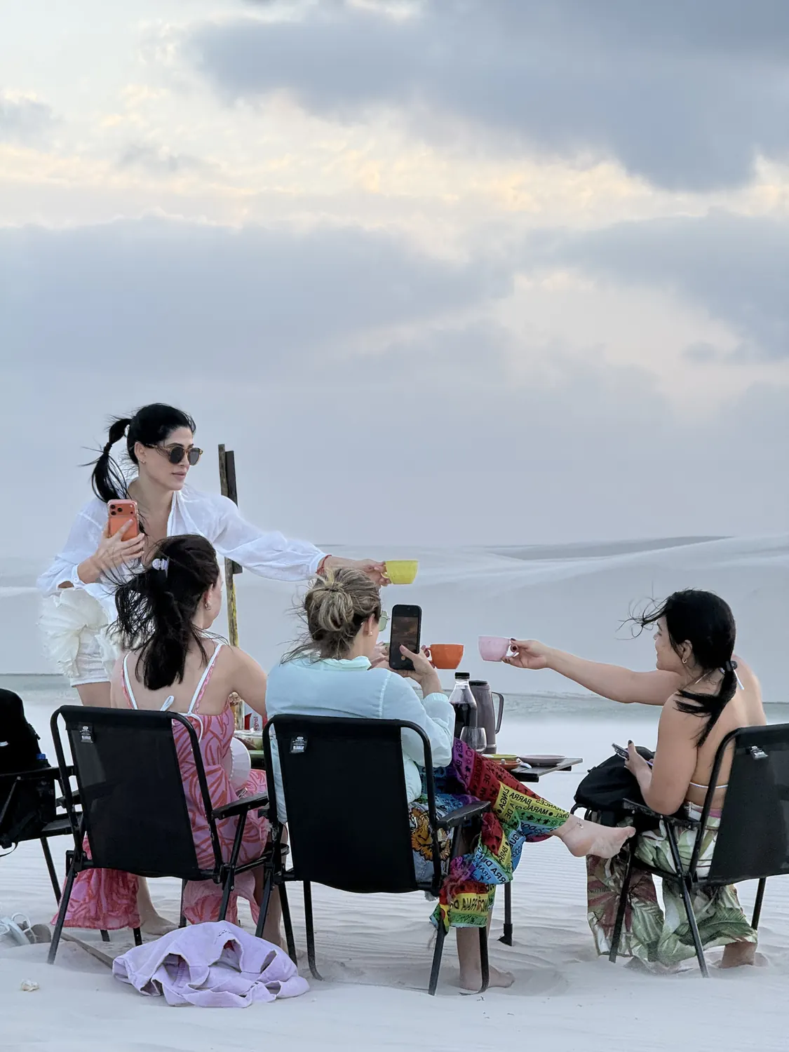 Café da manhã servido na duna, com o grupo brindando com as xícaras