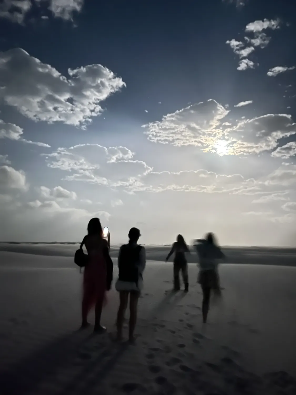 Grupo caminhando pelas dunas sob o luar, antes do nascer do sol
