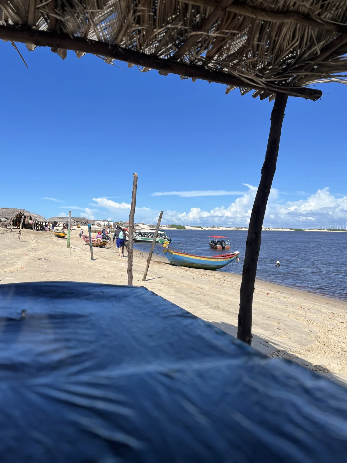 Praia do Caburé vista da sombra de uma barraca de palha, com os barcos na beira do rio