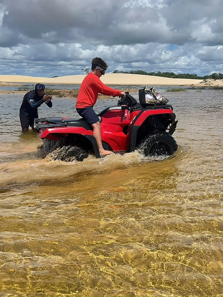 Visitante pilotando o quadriciclo por um trecho raso de lagoa, com o guia fotografando ao lado
