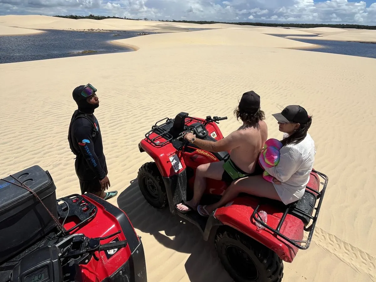 Casal em quadriciclo nas dunas dos Lençóis, acompanhado pelo guia, com lagoas ao fundo