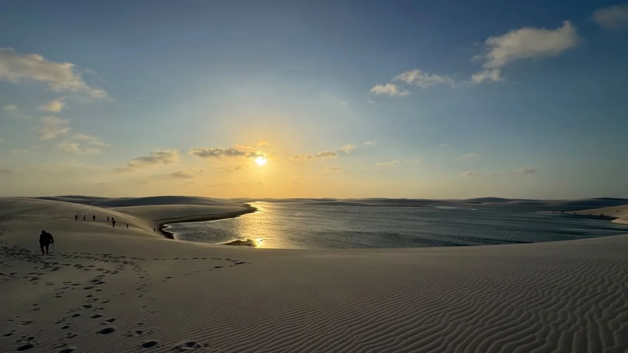 Pôr do sol sobre uma grande lagoa entre as dunas de Santo Amaro, com visitantes caminhando na areia
