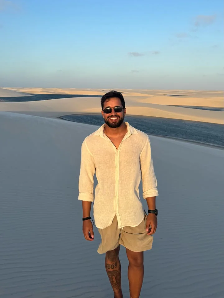 Visitante sorrindo no alto de uma duna, com lagoas e dunas ao fundo no fim de tarde