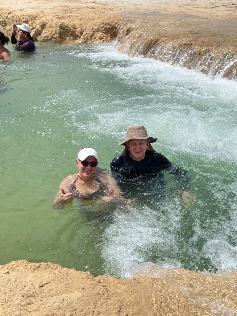 Casal em piscina natural com pequena cachoeira e rochas nos Lençóis Maranhenses