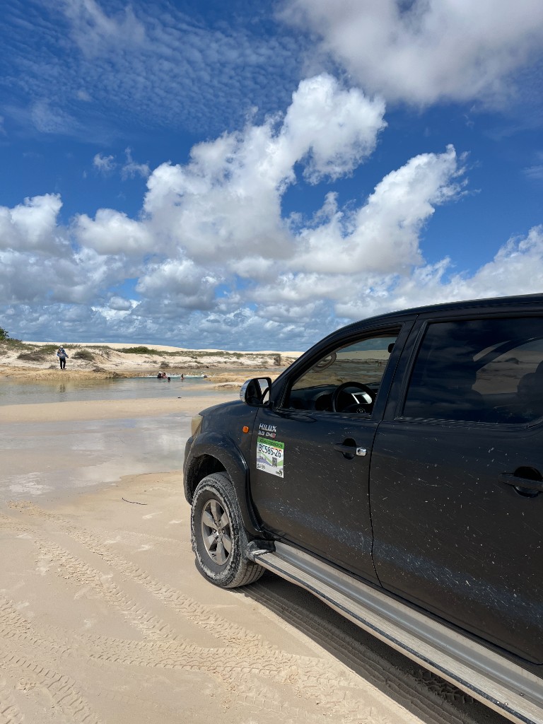 Veículo 4x4 em paisagem de areia, lagoa e dunas nos Lençóis Maranhenses